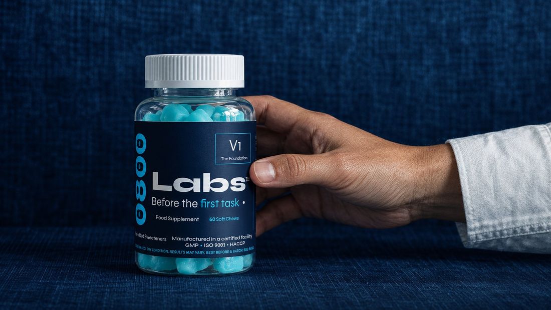 A hand reaching for a bottle of 0800Labs' V1 gummies against a navy textile background, the discontinued prototype from Field Test 001.