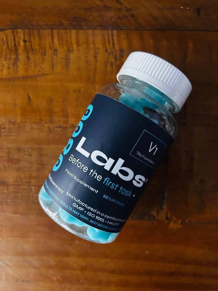 A single V1 gummy bottle on a wood desk surface, showing the 0800Labs V1 'Before the first task' label.